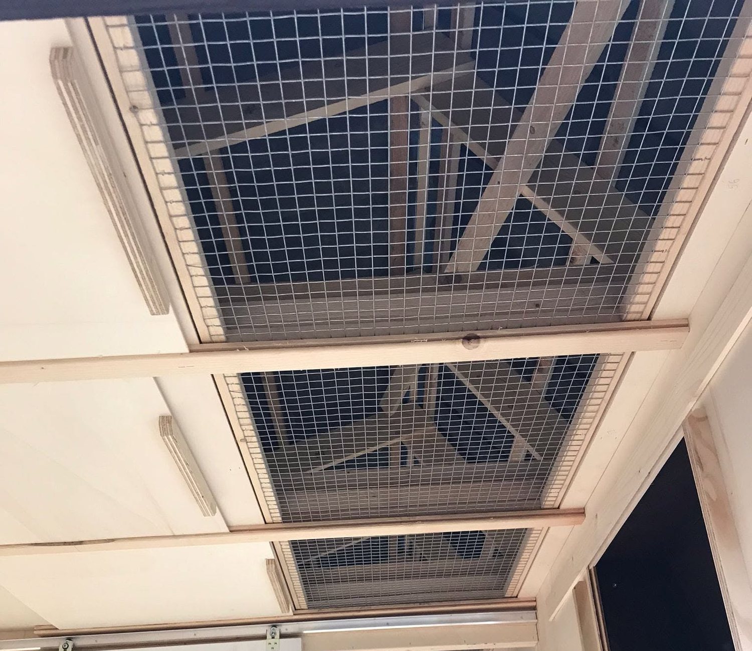 Plafond in een duivenhok van binnenuit gezien, met drie met gaas afgedekte openingen naar de kapruimte en houten schuiven in geleiders ernaast